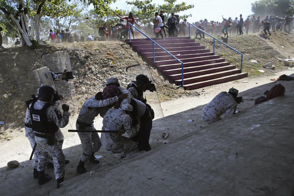 Mexican National Guards detain a Central American migrant, partially covered, as some migrants throw rocks at them after the group crossed from Guatemala to Mexico, near the bank of the Suchiate River near Ciudad Hidalgo, Mexico, Monday, Jan. 20, 2020. More than a thousand Central American migrants hoping to reach the United States marooned in Guatemala are walking en masse across a river leading to Mexico in an attempt to convince authorities there to allow them passage through the country. (AP Photo/Marco Ugarte)