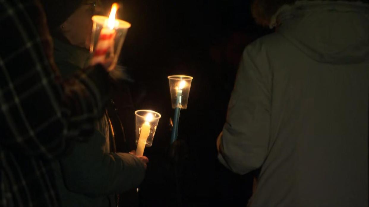 Community members hold candles by the Rideau River on Friday evening in memory of Ahmed Ahmed and Riley Cotter who died earlier this week. (CBC - image credit)