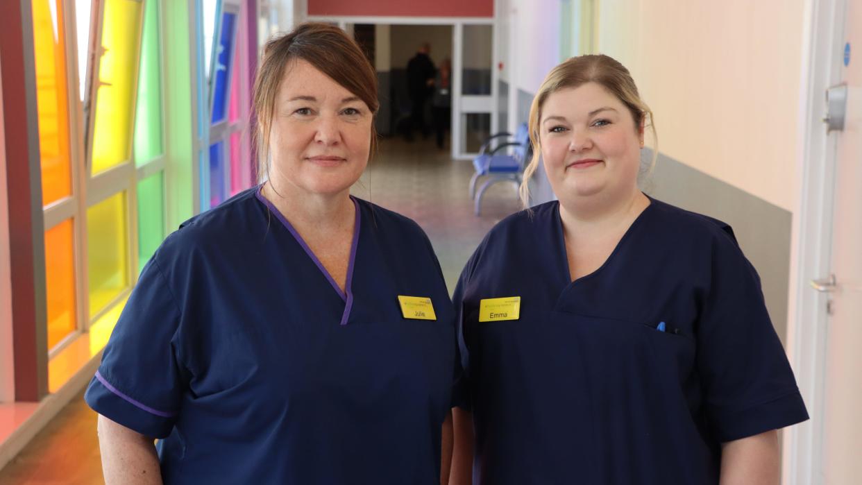 Brown haired woman in nurse's outfit smiling at camera next to blonde haired woman