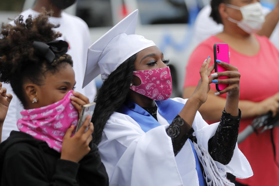 Masked graduates and guests take photos as the New Orleans Charter Science and Math High School class of 2020 holds a drive-in graduation ceremony as a result of the COVID-19 pandemic, outside Delgado Community College in New Orleans, Wednesday, May 27, 2020. Students and family got out of their cars to receive diplomas one by one, and then held a parade of cars through city streets. (AP Photo/Gerald Herbert)