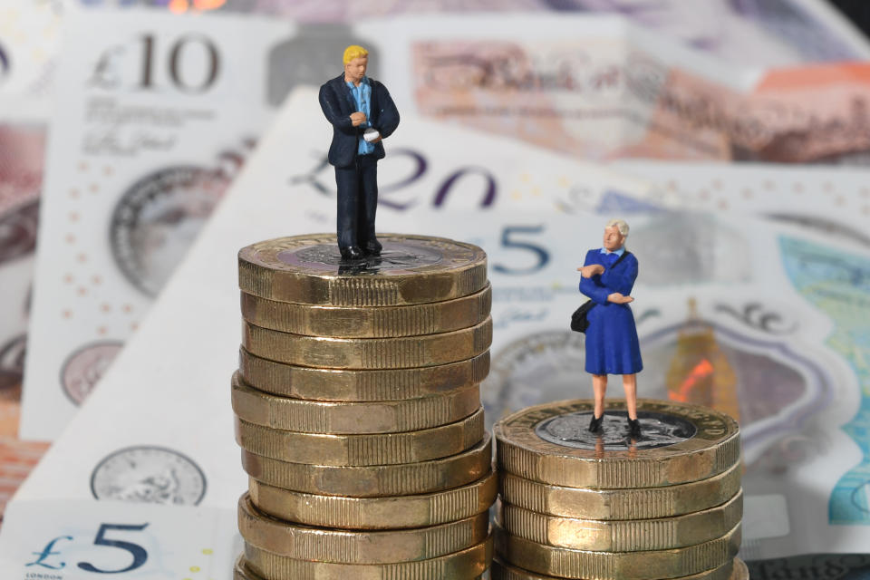 Models of a man and woman stand on a pile of coins and bank notes.