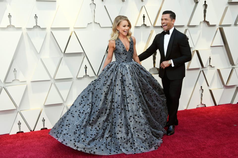 Kelly Ripa in a gorgeous design print dress looks stunning beside Mark Consuelos, who is dressed in a black suit, white inner T-shirt and pant to match