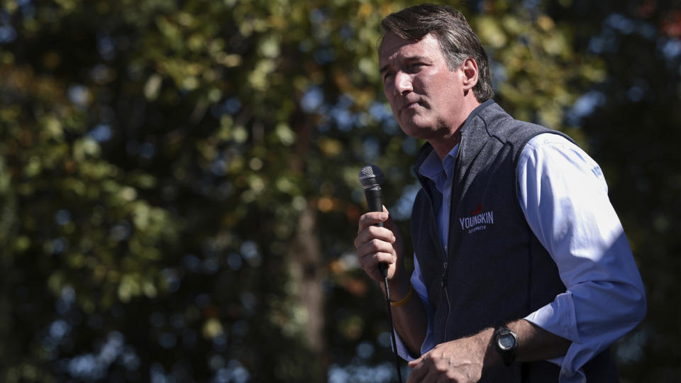 Glenn Youngkin stands holding a microphone in an outdoor setting.