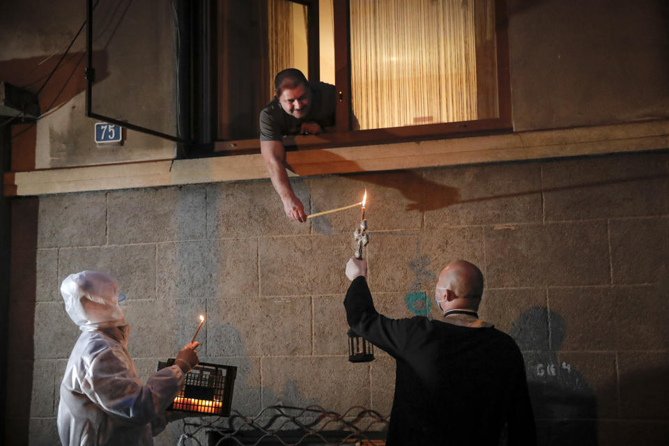 A man leans out his window to receive Holy Light from a priest in Bucharest, Romania, Saturday, April 18, 2020. Priests accompanied by volunteers distributed the candles ahead of the usual time, at midnight, as people observed the ban on gatherings in the week leading to the Orthodox Easter, as authorities try to limit the spread of the COVID-19 coronavirus. (AP Photo/Vadim Ghirda)