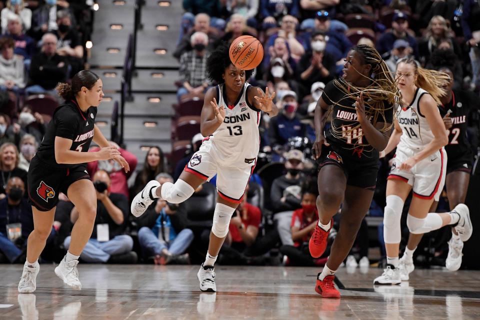 Connecticut's Christyn Williams (13) passes between Louisville's Mykasa Robinson (5) and Louisville's Olivia Cochran (44) in the first half of their game Sunday, Dec. 19, 2021, in Uncasville, Conn.