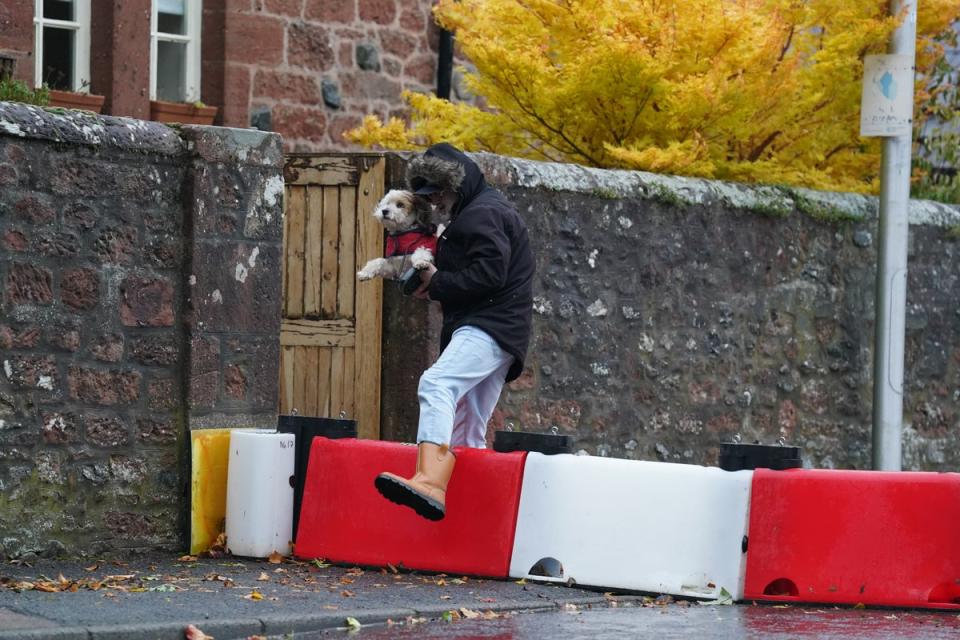 A man lifts his dog over a flood defence barrier erected on Church street in the village of Edzell (PA)