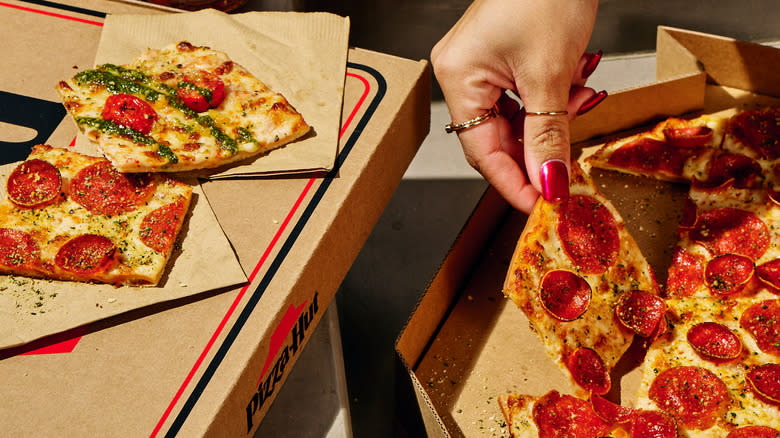 Person taking square pizza slice