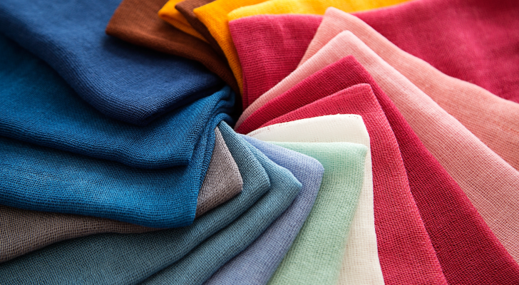 An array of fabric and textiles is arranged on a surface. The fabrics are of all colors; pinks, green, blues, yellows, and browns.