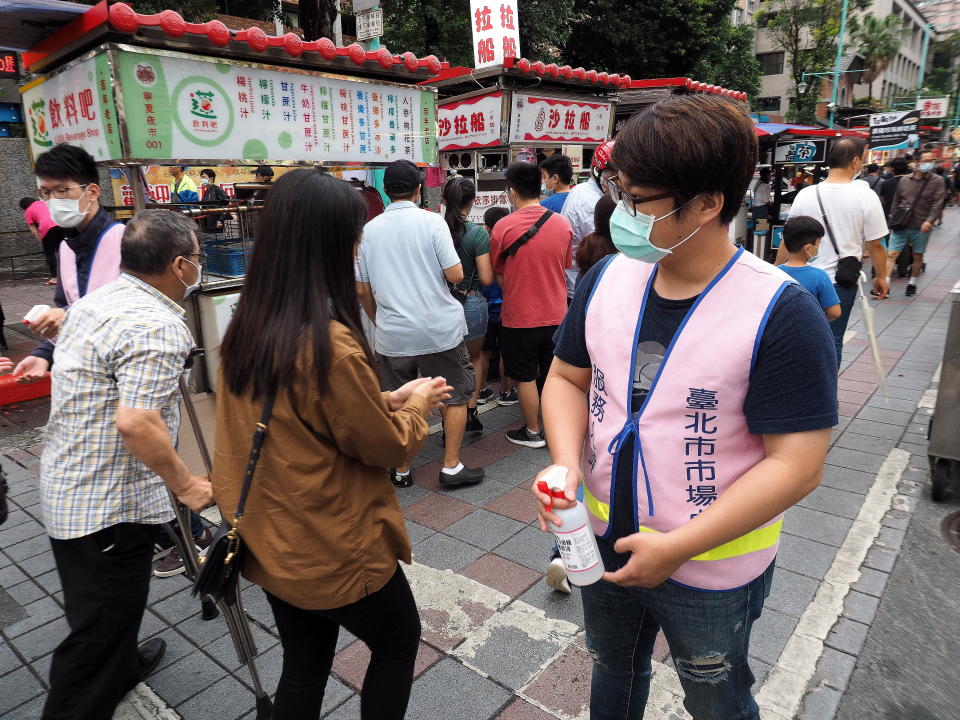 Two health workers stand ready to apply sanitising gel on people&#39;s hands at the Ningxia Night Market in Taipei, Taiwan, 22 May 2020. Source: EPA via AAP