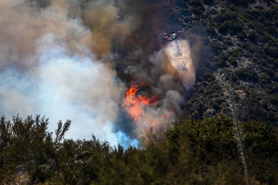 Flames and smoke rise from a wildfire as a helicopter drops water