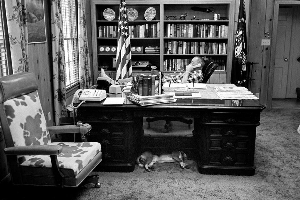 President Lyndon B. Johnson talks on the telephone while a beagle dozes under his desk in his Texas White House office at the LBJ Ranch on April 17, 1965.