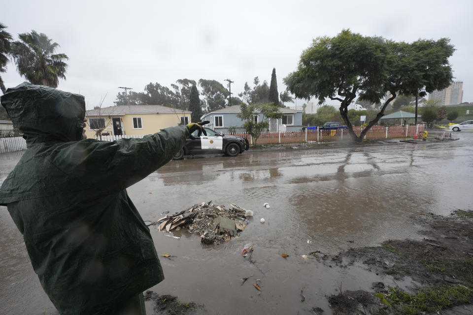 Ruben Gomez points along a partially flooded street as he breaks from clearing away mud and flood debris that engulfed his parents' home in the previous rainstorm as more rain falls Thursday, Feb. 1, 2024, in San Diego. Gomez has spent all of his time since the Jan. 22 storm shuttling between caring for his parents who were rescued by boat and later hospitalized that day, and trying to salvage what he can from the flooded home. Now, with more rain coming, Gomez worries the floodwaters may rise again in his parents' neighborhood. (AP Photo/Gregory Bull)