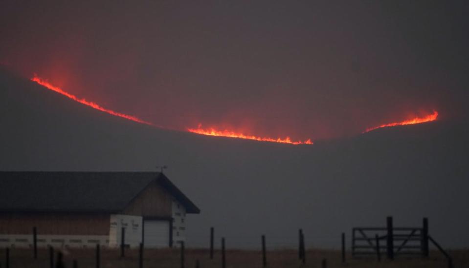 Fire lights up a ridge behind a farm.