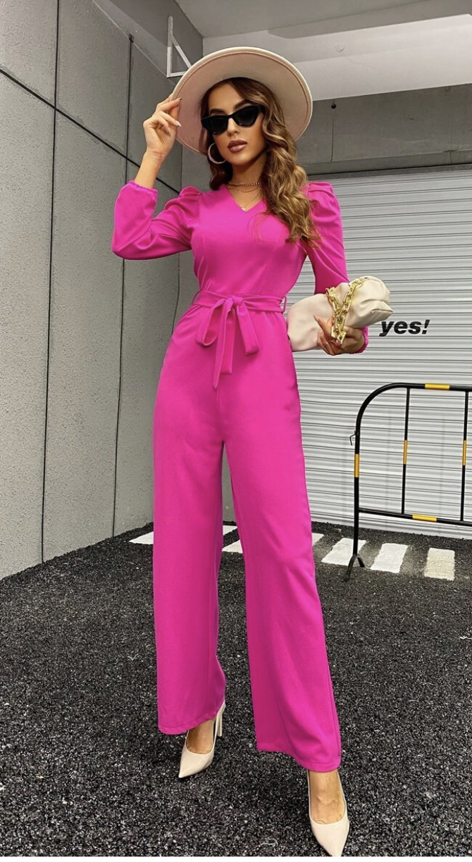 A tall model stands one leg forward in hot pink jumpsuit with race day hat and dark shades, one hand on hat and handbag in other