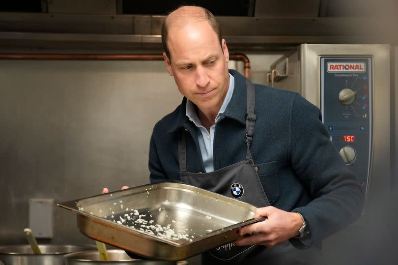 Prince William wearing a black apron holding a tray of chopped up celery