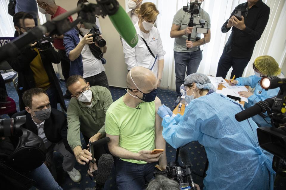 Germany's tourist Uwe Keim, center, wearing a face mask to protect against coronavirus gets the first shot of Russia's Sputnik V coronavirus vaccine in Moscow, Russia, Friday, April 16, 2021. Uwe Keim, 46-year-old software developer from Stuttgart, told The Associated Press after getting his jab that he isn't worried about depriving some Russian of their shot, as he believes "there are more vaccines available here in Russia than is demanded by the people here." (AP Photo/Pavel Golovkin)