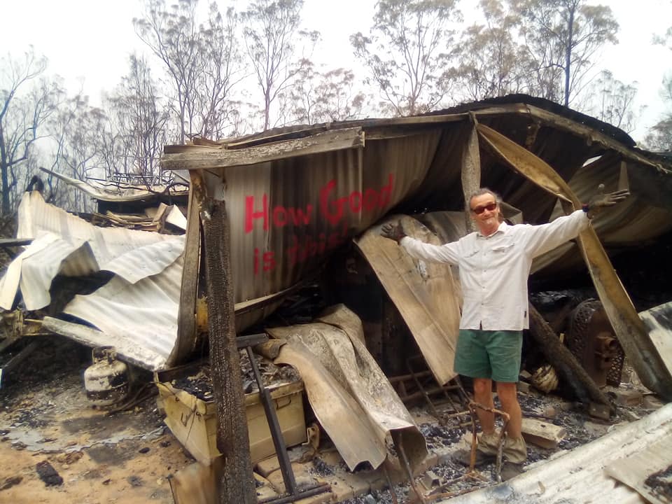 The Nymboida man stands with bushfire debris from his home. A message saying, "How good is this", is seen scrawled on a piece of corrugated iron.