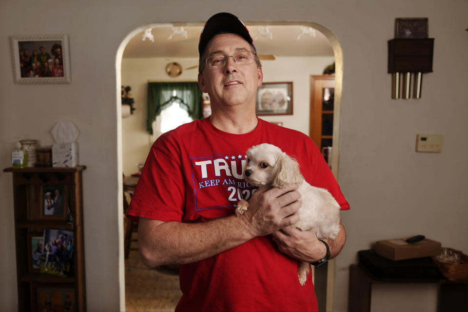 Jeff Butcher poses with Drizzly, the family dog, in his home in Celina, Ohio, Dec. 17, 2020. Butcher considered himself a non-political centrist before he came to admire Trump, who would "run the country like it was a business." (AP Photo/Mark Humphrey)