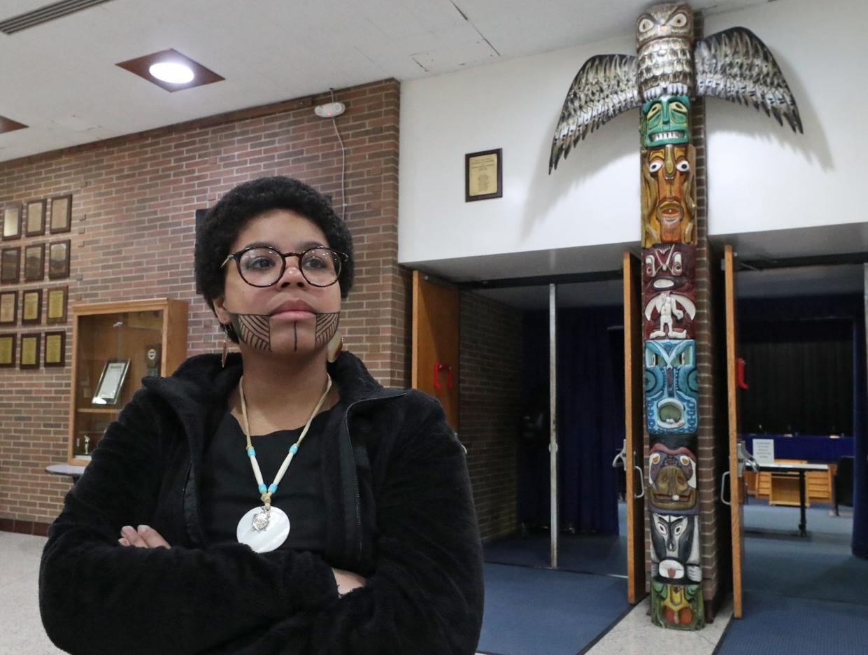 Copley High graduate Connie Becker, 19, who has a temporary Jagua tattoo on her face, stands near a totem pole outside of the entrance to the auditorium at Copley High School before a board of education meeting on Jan. 9. Becker, who identifies as Taino, the historic indigenous people of the Caribbean, has spoken in favor of changing the Copley mascot.