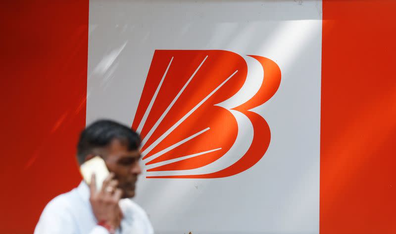 A man talks on mobile phone in front of the Bank of Baroda logo in New Delhi