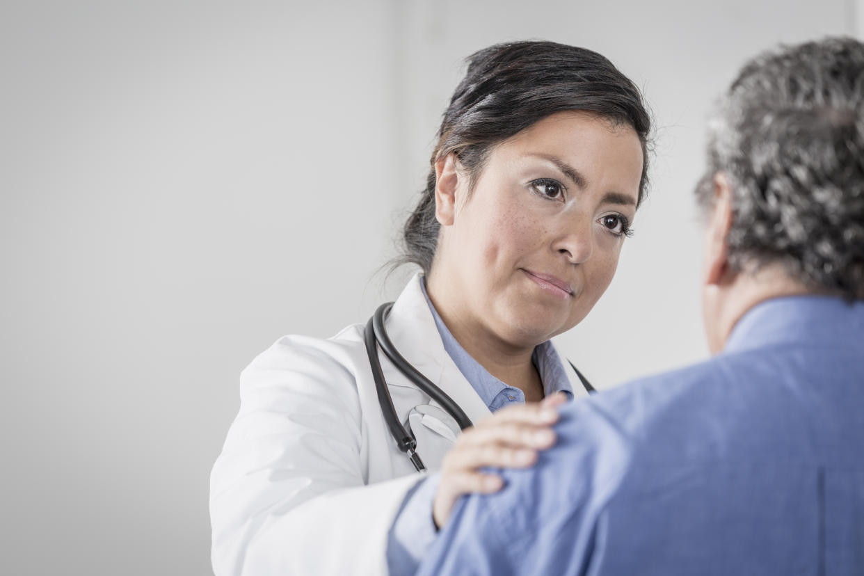 A doctor puts her hand on an older patient's shoulder.