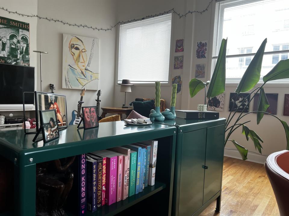 Green living room cabinets behind the couch with books lined up, picture frames, and two candlesticks.