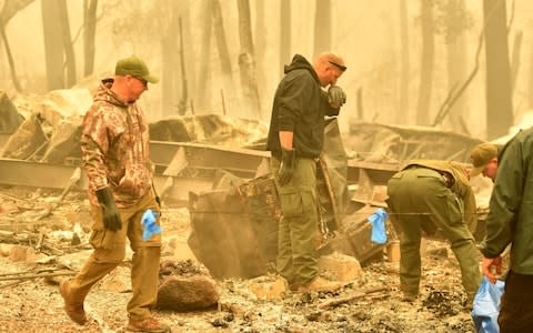 Yuba and Butte County Sheriff officers react as they discover a body at a burned out residence after the Camp fire tore through the area in Paradise - Credit: AFP