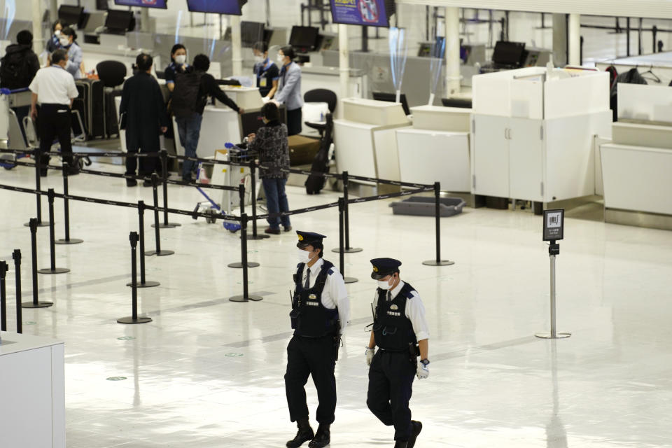 Police officers walk around on the departure ticketing counter floor at the Narita International Airport in Narita, east of Tokyo, Thursday, Dec. 2, 2021. Going further than many other countries in trying to contain the virus, Japan has banned foreign visitors and asked international airlines to stop taking new reservations for all flights arriving in the country until the end of December. (AP Photo/Hiro Komae)