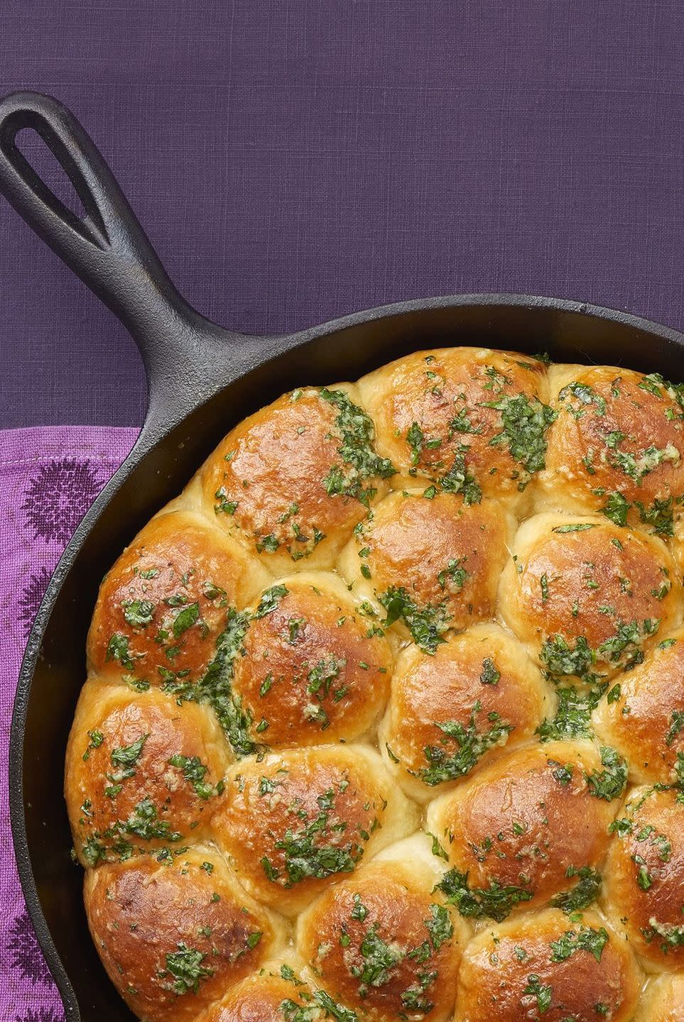 skillet dinner rolls with garlic herb butter in cast iron skillet on purple linen