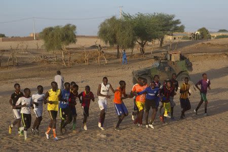 Soccer players run in front of a French armoured vehicle from Operation Barkhane on patrol in Timbuktu, November 5, 2014. REUTERS/Joe Penney