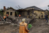 An elderly worker arrives with a broom at a crater caused by a rocket strike on a house in Kramatorsk, Donetsk region, eastern Ukraine, Friday, Aug. 12, 2022. There were no injuries reported in the strike. (AP Photo/David Goldman)