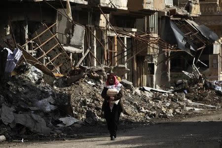 FILE PHOTO:A man holds bread as he walks along a damaged street filled with debris in Deir al-Zor, eastern Syria February 19, 2014. REUTERS/Khalil Ashawi/File Photo