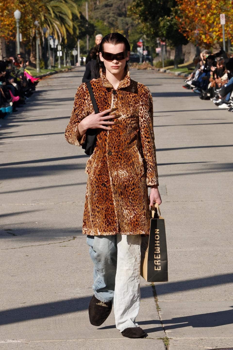 A model, carrying a branded Erewhon grocery bag, walks the Balenciaga Fall 2024 runway in Los Angeles.