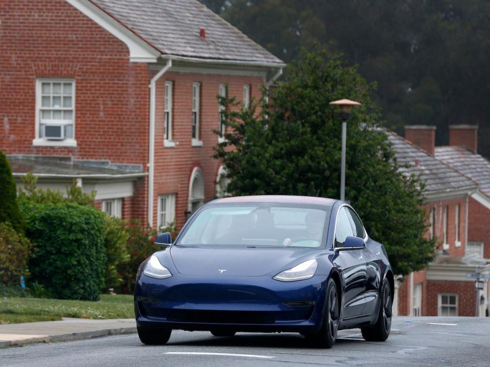 A Tesla model 3 drives on past a house.