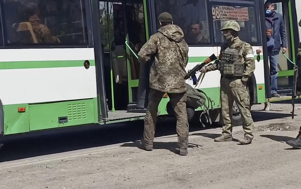 In this photo taken from video released by the Russian Defense Ministry Press Service on Wednesday, May 18, 2022, Russian servicemen watch Ukrainian servicemen boarding a bus after they leaved the besieged Azovstal steel plant in Mariupol, Ukraine.(Russian Defense Ministry Press Service via AP)