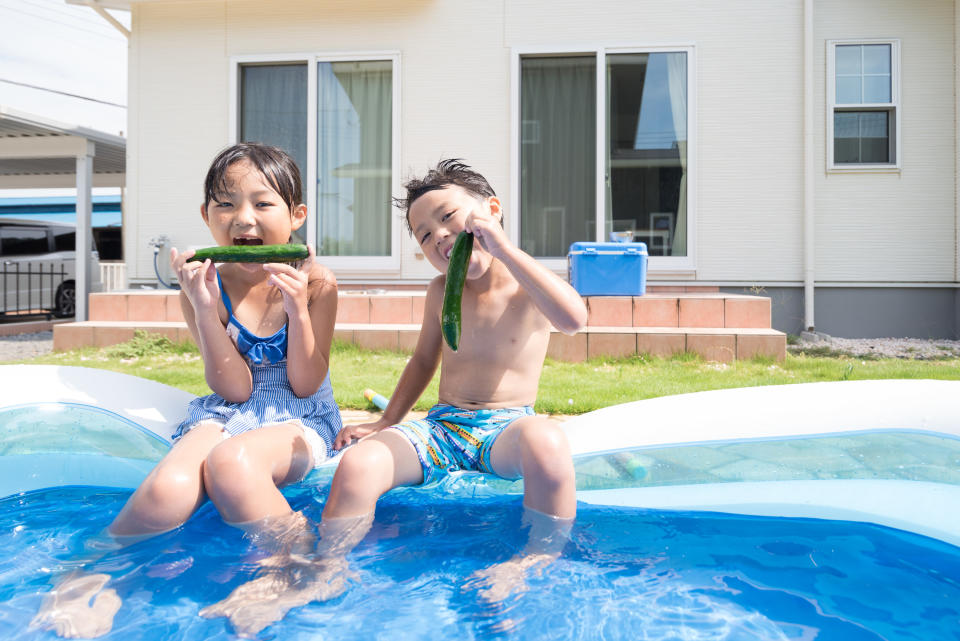 asian kids sitting in an inflatable pool eating cucumbers