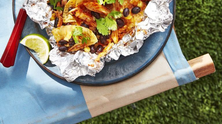 chicken and black bean nachos on a piece of foil on a blue stoneware plate with a fork