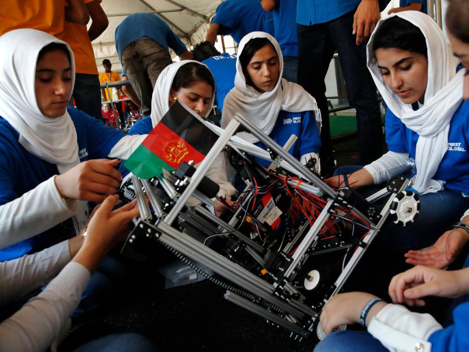 Four Afghan members of a robotics team make repairs on a robot.