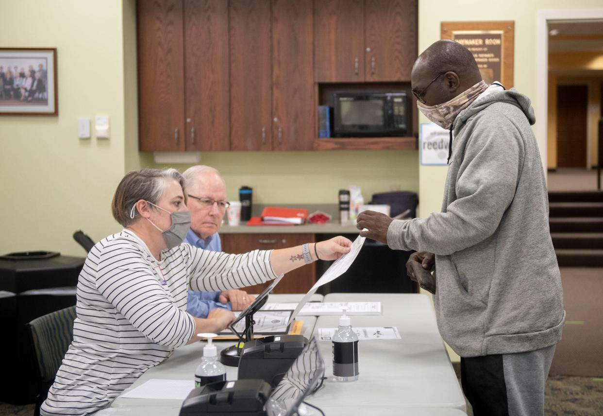 Christina West, with Tim Calfee, hands a ballot to Dennis Wiliiams at Reed Memorial Library in Ravenna.