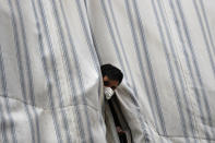 In this Saturday, May 23, 2020 photo, a Bangladeshi worker looks from behind a curtain of his apartment balcony in a building where dozens of foreign workers living in overcrowded apartments have tested positive with the coronavirus, in Beirut, Lebanon. Some 250,000 registered migrant laborers in Lebanon — maids, garbage collectors, farm hands and construction workers — are growing more desperate as a crippling economic and financial crisis sets in, coupled with coronavirus restrictions. With no functioning airports and exorbitant costs of repatriation flights, many are trapped, unable to go home. (AP Photo/Hussein Malla)