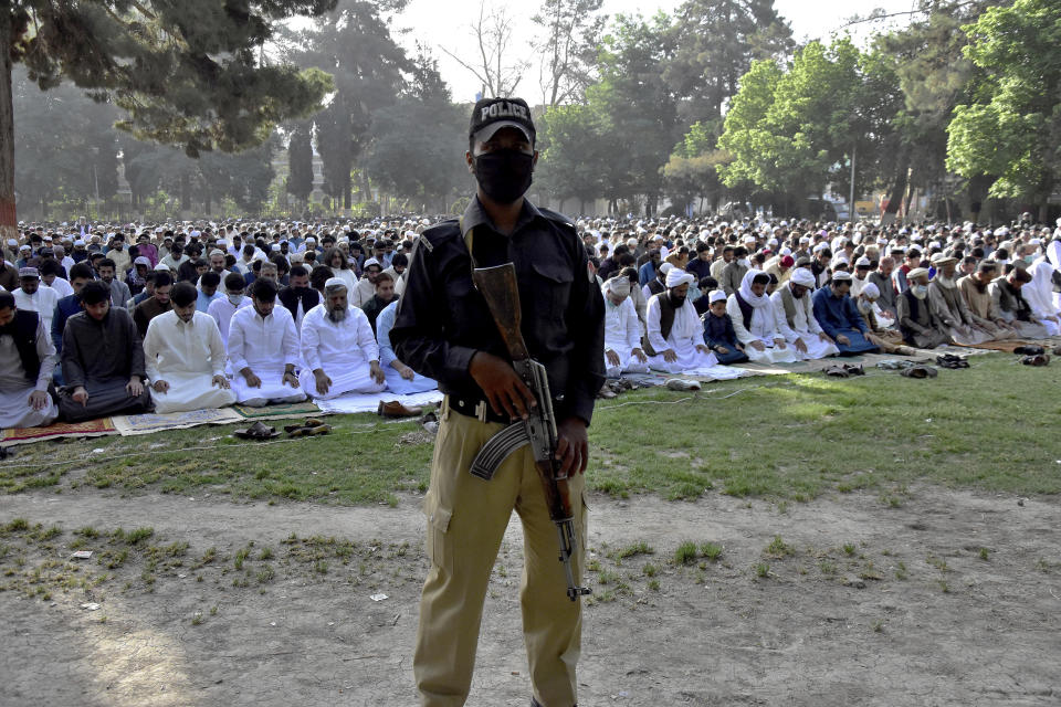 A police officer stands guard while Muslims perform an Eid al-Fitr prayer at a ground, in Quetta, Pakistan, Thursday, May 13, 2021. Millions of Muslims across the world are marking a muted and gloomy holiday of Eid al-Fitr, the end of the fasting month of Ramadan - a usually joyous three-day celebration that has been significantly toned down as coronavirus cases soar. (AP Photo/Arshad Butt)