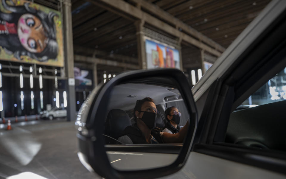 Visitors take in an art exhibit from inside a car as they drive through a warehouse displaying paintings and photos in Sao Paulo, Brazil, Friday, July 24, 2020, amid the new coronavirus pandemic. Galleries, cinemas, theaters and museums are closed due to the restrictive measures to avoid the spread of COVID-19, but a group of artists and a curator found a way to overcome the restrictions to share their art with the residents of Brazil’s largest city. (AP Photo/Andre Penner)