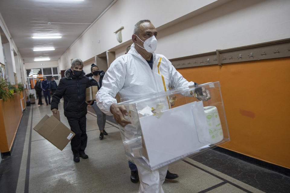 Election official in protective clothes carries a ballot box and election material as the polls open for parliamentary elections in the town of Bankya near capital Sofia, Bulgaria on Sunday, April 4, 2021. Bulgarians are heading to the polls on Sunday to cast ballots for a new parliament after months of anti-government protests and amid a surge of coronavirus infections. (AP Photo/Visar Kryeziu)