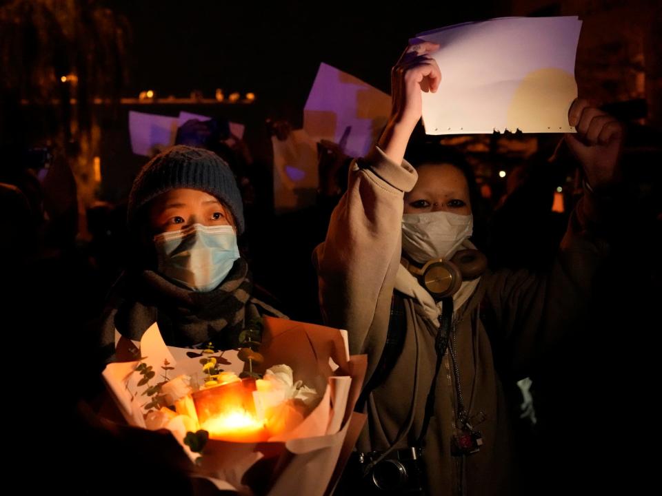 Protesters hold up blank papers and hold flowers and candles as they march in protest in Beijing