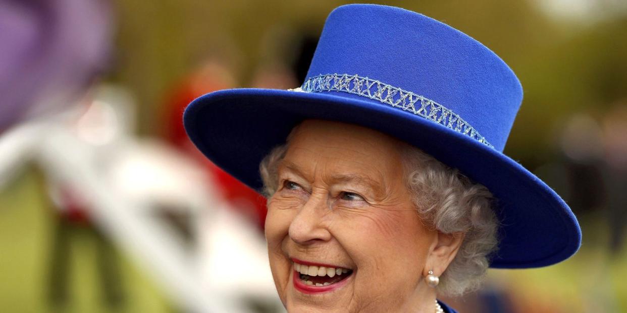 queen elizabeth ii laughing whilst wearing a matching blue hat and jacket