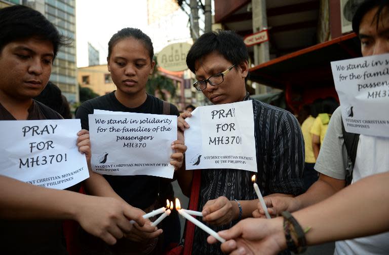 Students light candles as they hold placards in solidarity with families of the passengers of the missing Malaysia Airlines flight MH370 plane during a vigil at the university belt in Manila