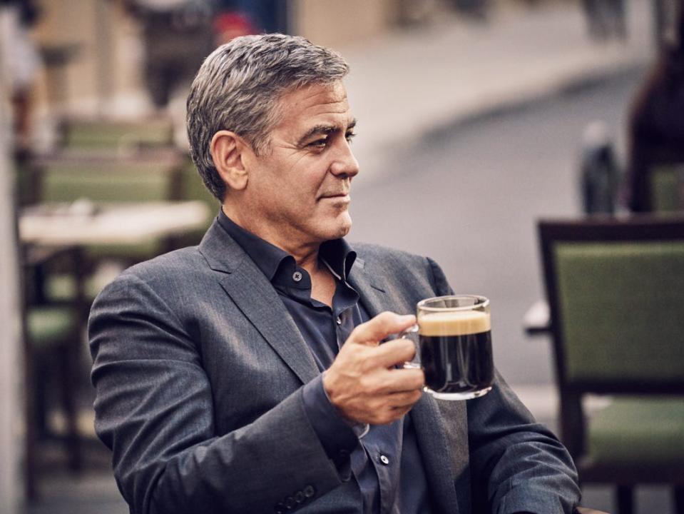 George Clooney in a gray jacket holding a coffee