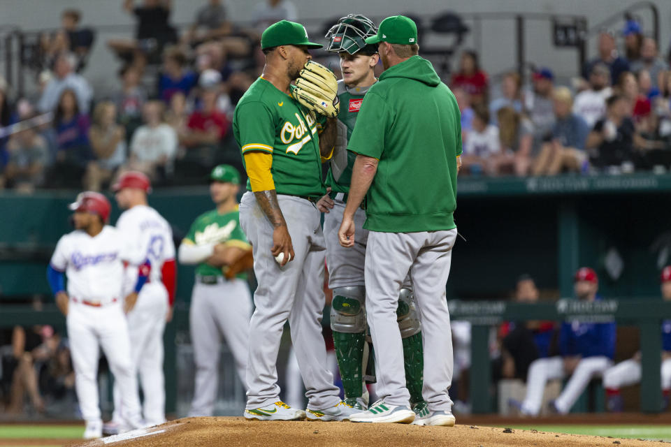 Oakland Athletics starting pitcher Frankie Montas, foreground left, catcher Sean Murphy, foreground center, and pitching coach Scott Emerson, right, talk on the mound during the first inning of a baseball game against the Texas Rangers, Monday, June 21, 2021, in Arlington, Texas. (AP Photo/Sam Hodde)