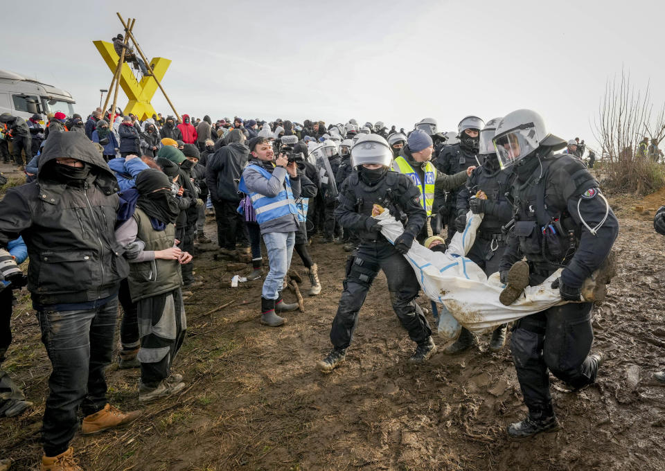 Police officers carry a demonstrator to clear a road at the village Luetzerath near Erkelenz, Germany, Tuesday, Jan. 10, 2023. The village of Luetzerath is occupied by climate activists fighting against the demolishing of the village to expand the Garzweiler lignite coal mine near the Dutch border. (AP Photo/Michael Probst)