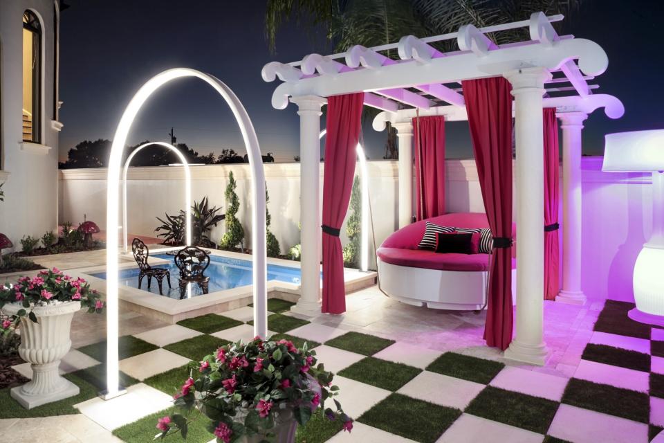 This 2019 photo provided by Ryan Hughes of Ryan Hughes Design Build shows an outdoor space at a home in Florida. Tampa-based designer Hughes took inspiration from the homeowner's daughter's love of Alice in Wonderland to create a playful, over-the-top outdoor space complete with unique lighting effects, a hanging bed and oversized checkerboard. (Joe Traina/Ryan Hughes via AP)